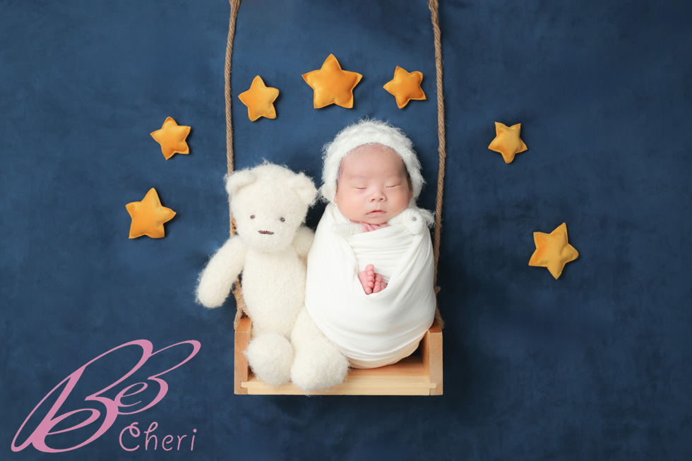 ブランコに乗るニューボーンフォト。白いクマのぬいぐるみと星の飾りに囲まれた愛らしい男の子の赤ちゃん。東京都多摩市での出張撮影。